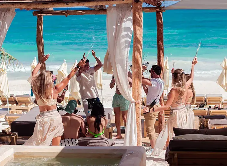 Vibrant beach club celebration in Tulum with guests enjoying turquoise waters and beachfront luxury