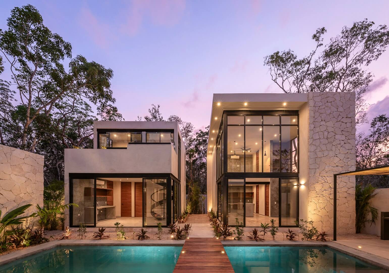 Modern Tulum villa at twilight with infinity pool, contemporary architecture, stone walls, and warm lighting surrounded by jungle